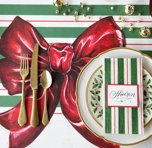 Christmas-themed place setting with red bow, gold cutlery, and holly design on a striped tablecloth.