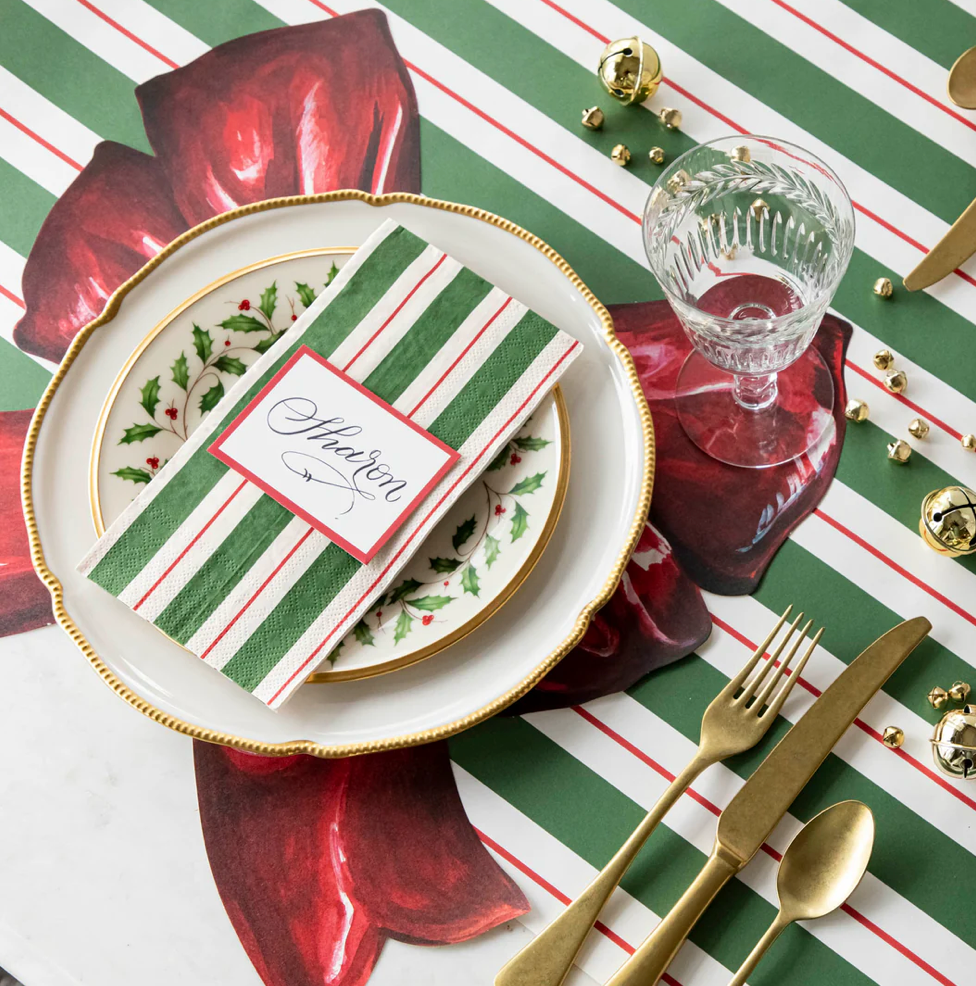 Christmas-themed table setting with red and green striped tablecloth, gold cutlery, and decorative name card.