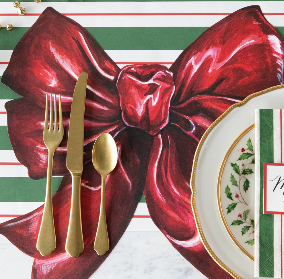 Christmas-themed place setting with gold cutlery, a red bow, and a striped background.