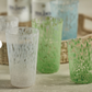 Set of three textured glass tumblers in white, green, and blue on a textured surface.