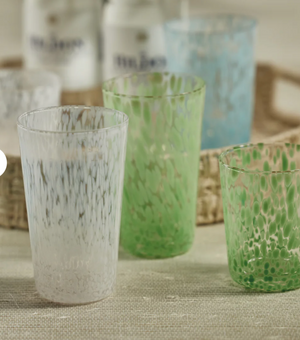 Set of three textured glass tumblers in white, green, and blue on a textured surface.