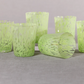 Set of green textured glass candle holders on a gray surface