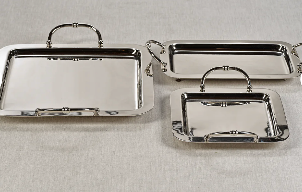 Set of three silver trays with handles on a light gray background