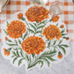 Floral placemat with orange marigold flowers on a checkered tablecloth.