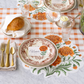 Decorative table setting with floral placemats, cutlery, and bread on a checkered tablecloth.