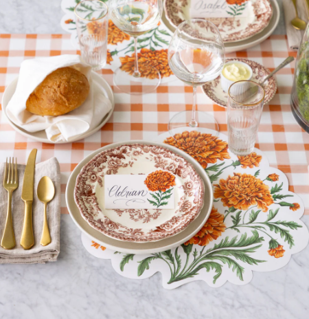 Decorative table setting with floral placemats, cutlery, and bread on a checkered tablecloth.