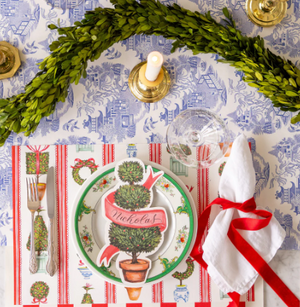 Decorative Christmas table setting with a topiary-themed plate, garland, and red ribbon.