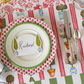 Decorative table setting with a place card, plates, and cutlery on a patterned tablecloth.