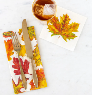 Table setting with fall-themed napkins, fork, knife, and cup of iced coffee on a white surface.