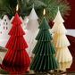 Three Christmas tree-shaped candles in red, green, and white on a reflective surface with a blurred background.