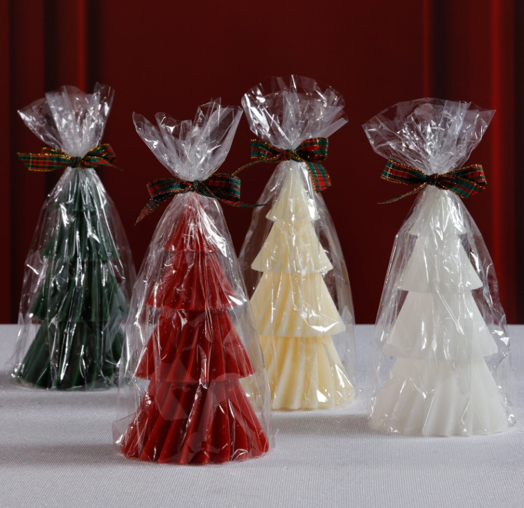 Four tree-shaped candies in red, green, white, and yellow, each wrapped in clear cellophane with decorative ribbons against a red background.
