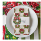Christmas-themed napkin with wreath design on a white plate with a 'Noel' card.