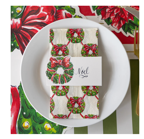 Christmas-themed napkin with wreath design on a white plate with a 'Noel' card.