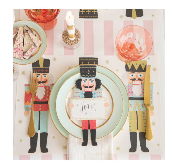 Table setting with nutcracker-themed placemats and cutlery on a striped tablecloth.