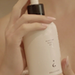 Hand holding a bottle of scented body oil with a pump.