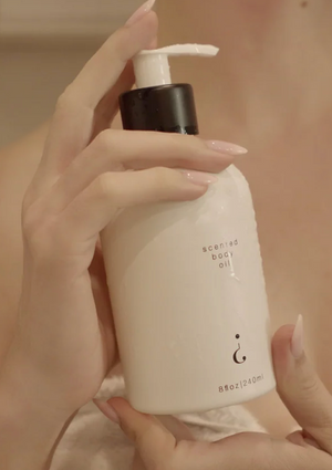 Hand holding a bottle of scented body oil with a pump.