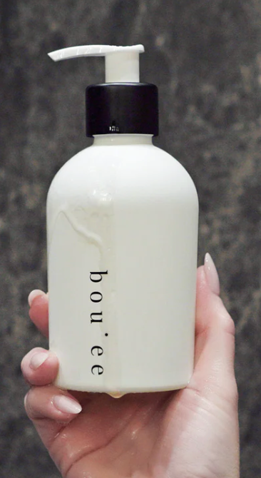 Hand holding a white bottle with a black pump labeled 'bouee' against a dark background