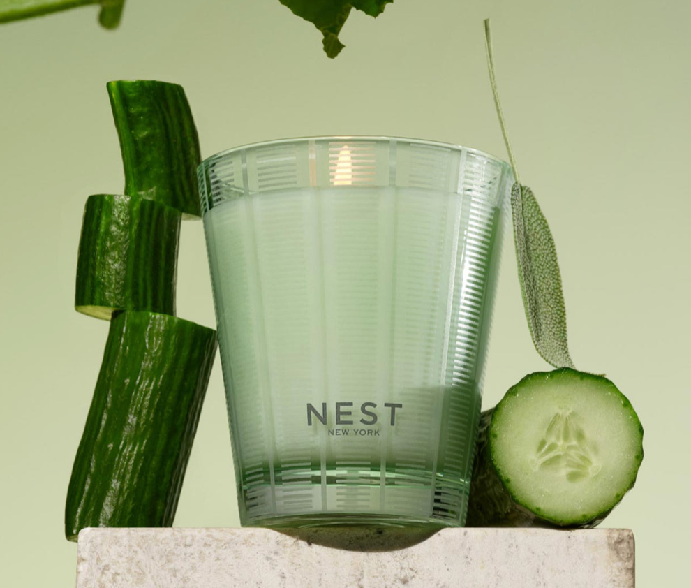 Clear glass with 'NEST New York' branding surrounded by sliced cucumbers on a light green background
