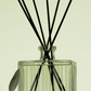 Clear diffuser bottle with black sticks and 'Nest' branding on a light background
