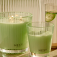 Two green candles labeled 'NEST' on a reflective surface with a blurred background.
