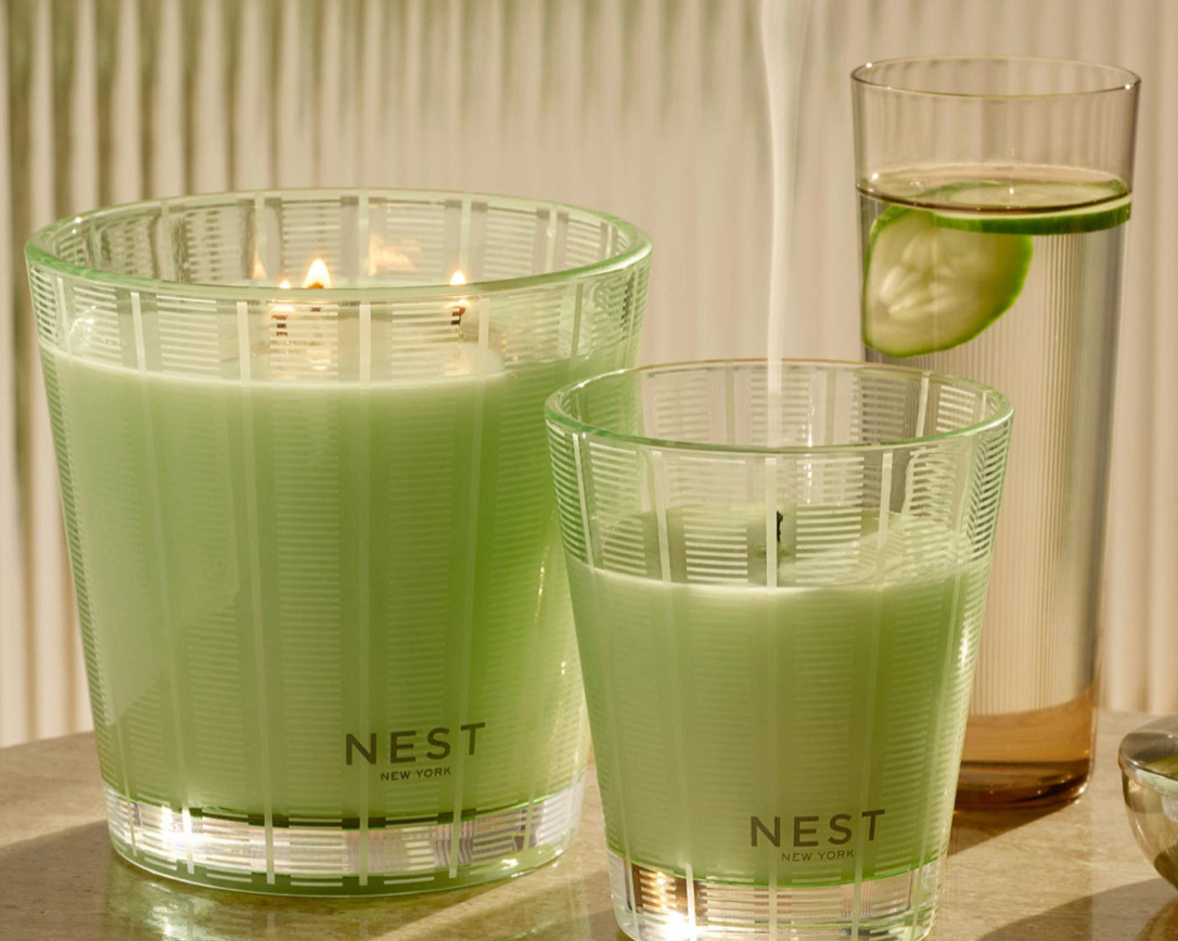 Two green candles labeled 'NEST' on a reflective surface with a blurred background.