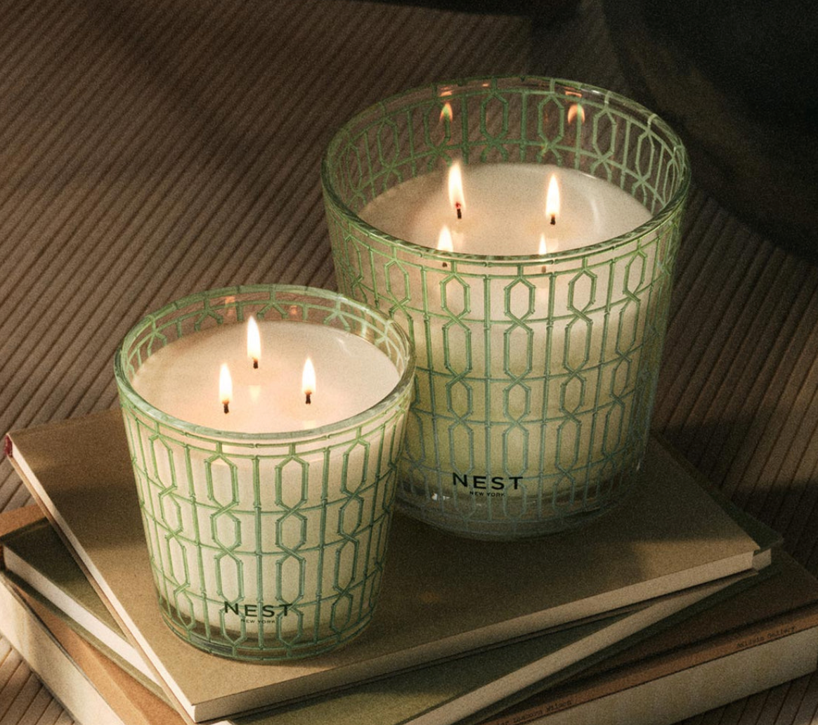 Two lit candles in green patterned containers on a surface with a striped background