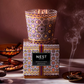 Decorative candle with intricate patterns and a matching box labeled 'NEST' on a dark background.