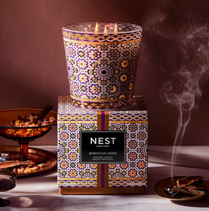 Decorative candle with intricate patterns and a matching box labeled 'NEST' on a dark background.
