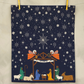 Nativity scene with angels and stars on a dark blue background, hanging on a line.