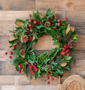 Christmas wreath with green leaves, red berries, and pinecones on a wooden background