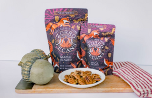 Two packages of 'Zorro Pecans' on a wooden board with a plate of pecans and a gourd.