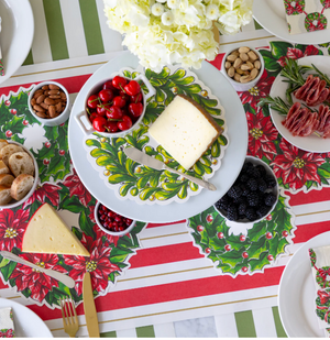 Dessert table setting with Christmas-themed placemats, cheese, and fruit on a white table.