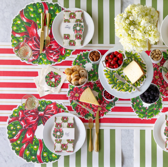 Christmas-themed table setting with wreath placemats and striped tablecloth.