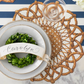 Decorative place setting with a wreath, name card, and woven placemat on a striped background.