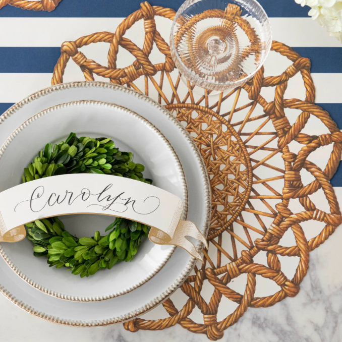 Decorative place setting with a wreath, name card, and woven placemat on a striped background.
