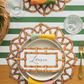 Decorative table setting with woven placemat, name card, and striped tablecloth.