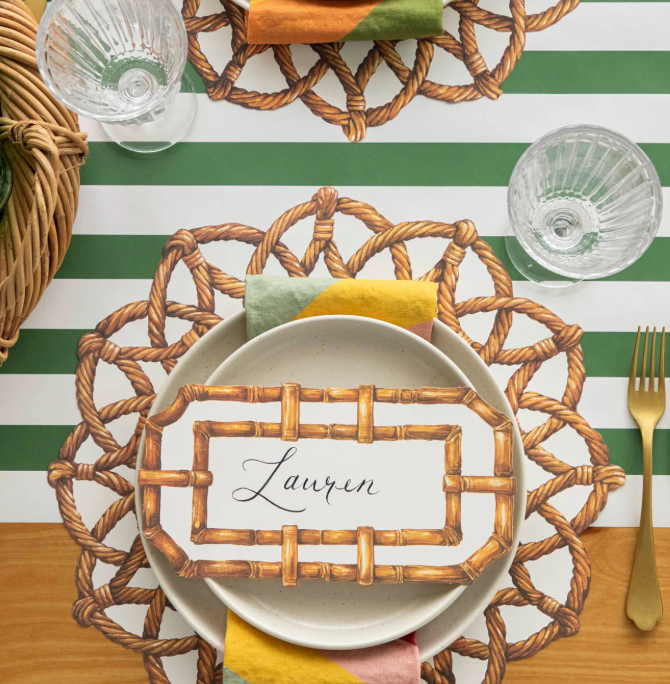 Decorative table setting with woven placemat, name card, and striped tablecloth.