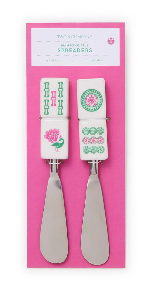 Two cheese spreaders with decorative handles on a pink packaging background