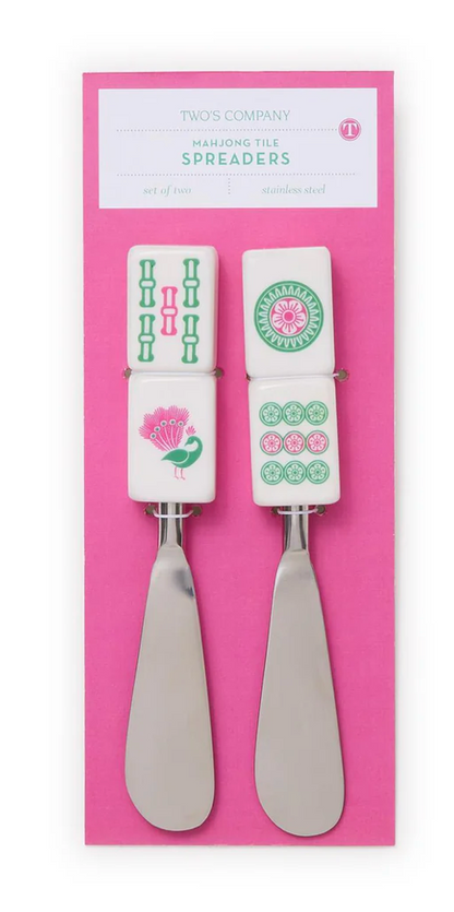 Two cheese spreaders with decorative handles on a pink packaging background