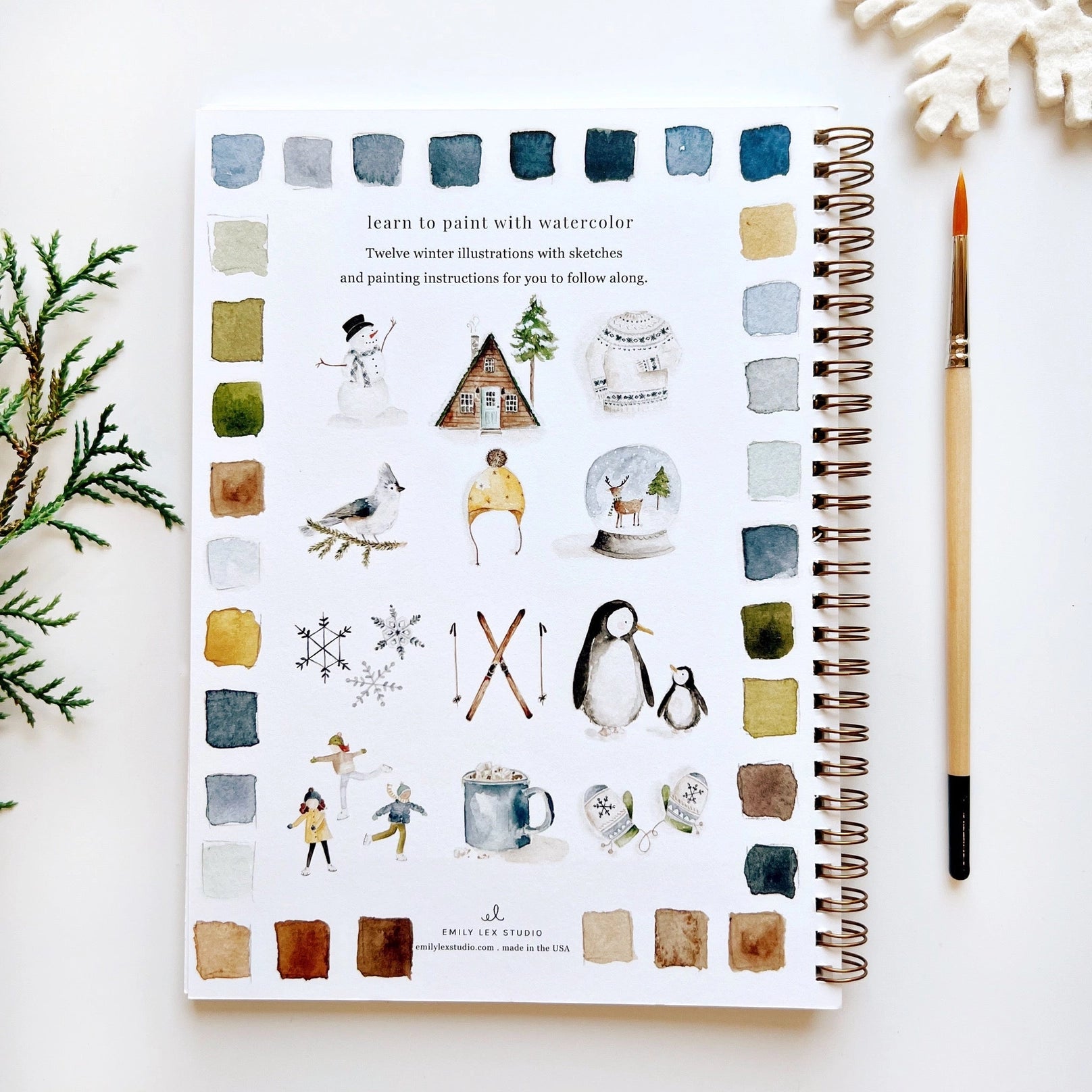 Notebook with watercolor illustrations on a white surface with a paintbrush and decorative elements.